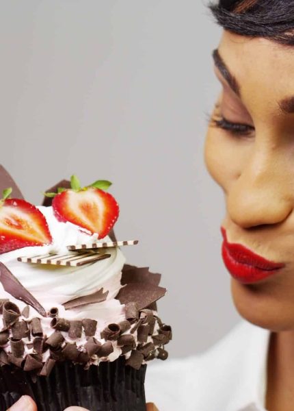 Black woman admiring a fancy dessert cupcake with chocolate and strawberries